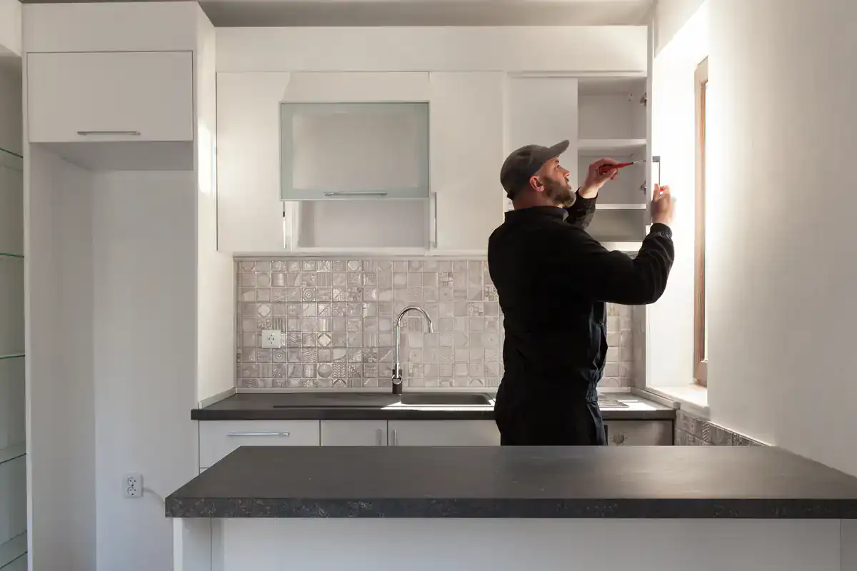 Someone adjusts a cabinet hinge in a bright kitchen during cabinet restoration Suffolk County.