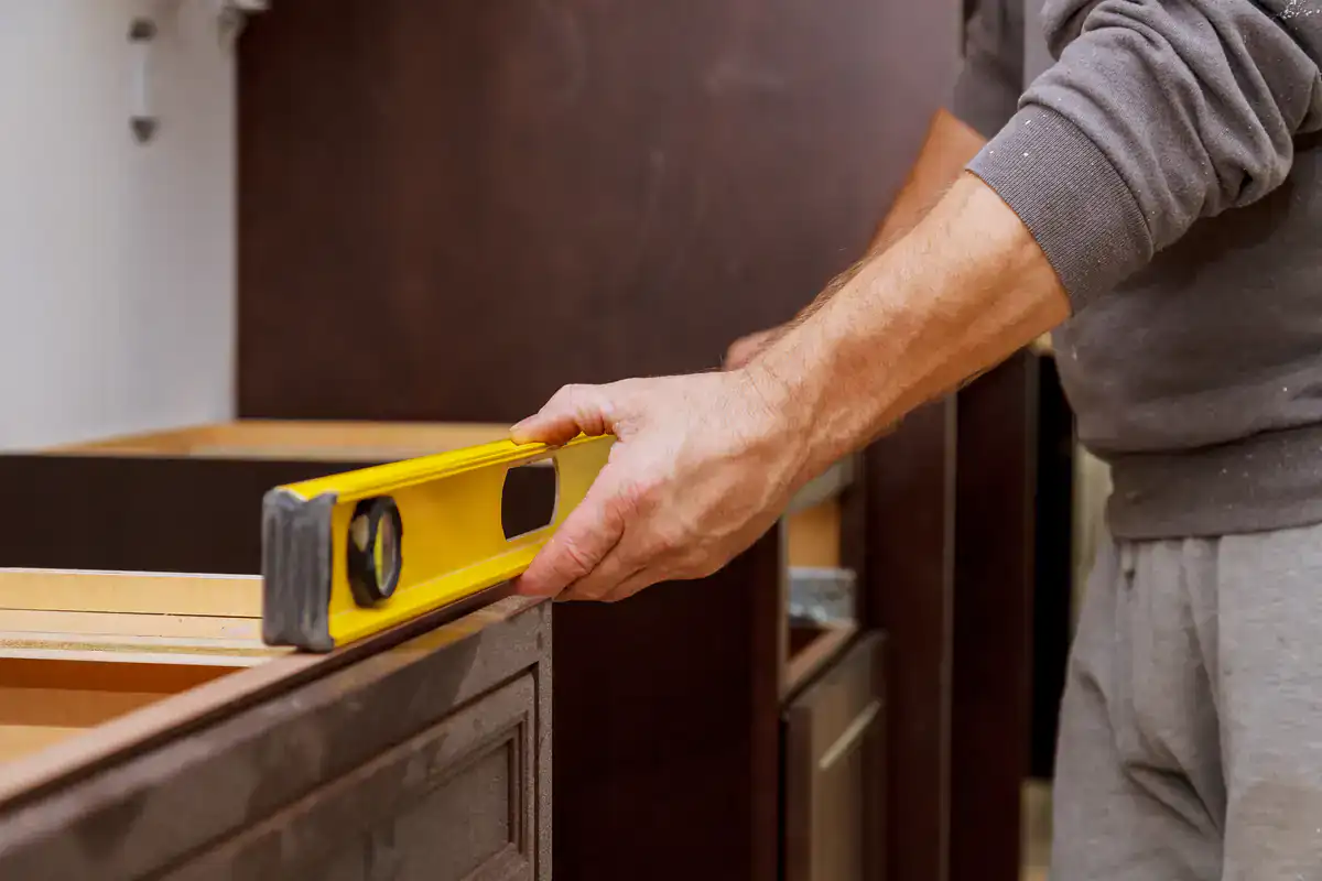 A person checks cabinet restoration in Suffolk County using a yellow spirit level in a kitchen remodel.