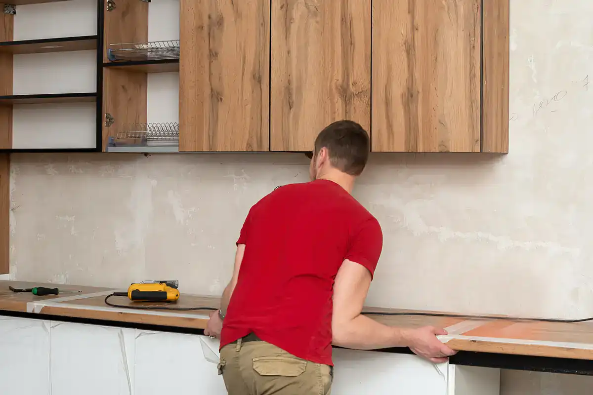 Man in red shirt installs wood countertop in NY kitchen, showing commercial millwork installation skills.