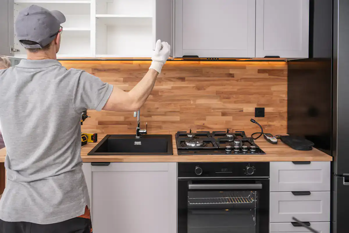 A person wearing gloves installs a kitchen cabinet above a stove, showcasing millwork installation skills.
