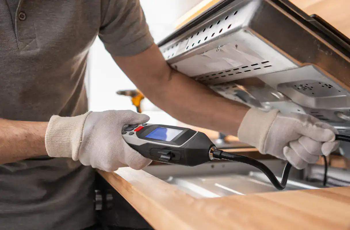 A gloved person in NY checks an appliance with a handheld device on wooden countertops in Suffolk County.