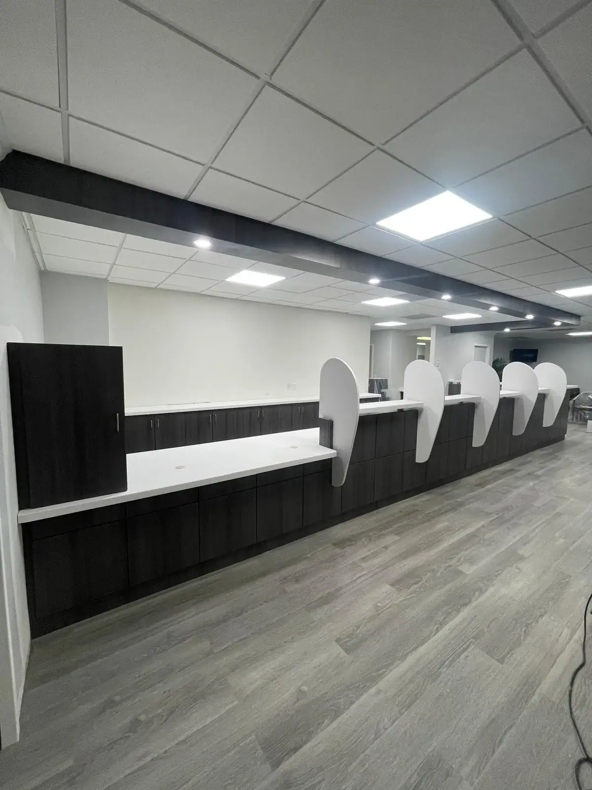 A modern NY office reception counter features white dividers, dark cabinets, and bright ceiling lights.